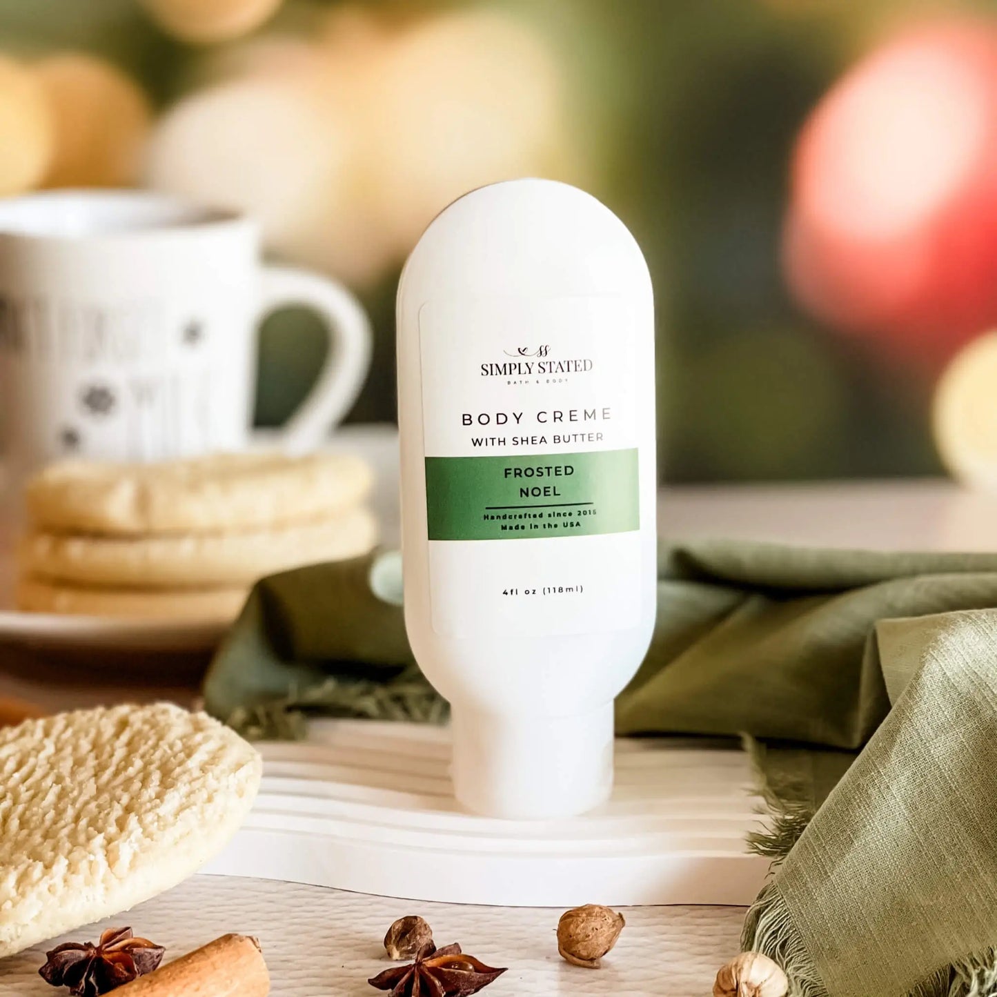 Body cream bottle labeled 'Frosted Noel' on a wooden surface with cookies and spices.